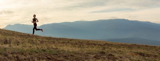 Female runner in open field with mountains in the background