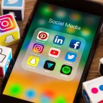 Picture of an iphone surrounded by cubes with social media icons. A 'social media' app folder open on the phone screen